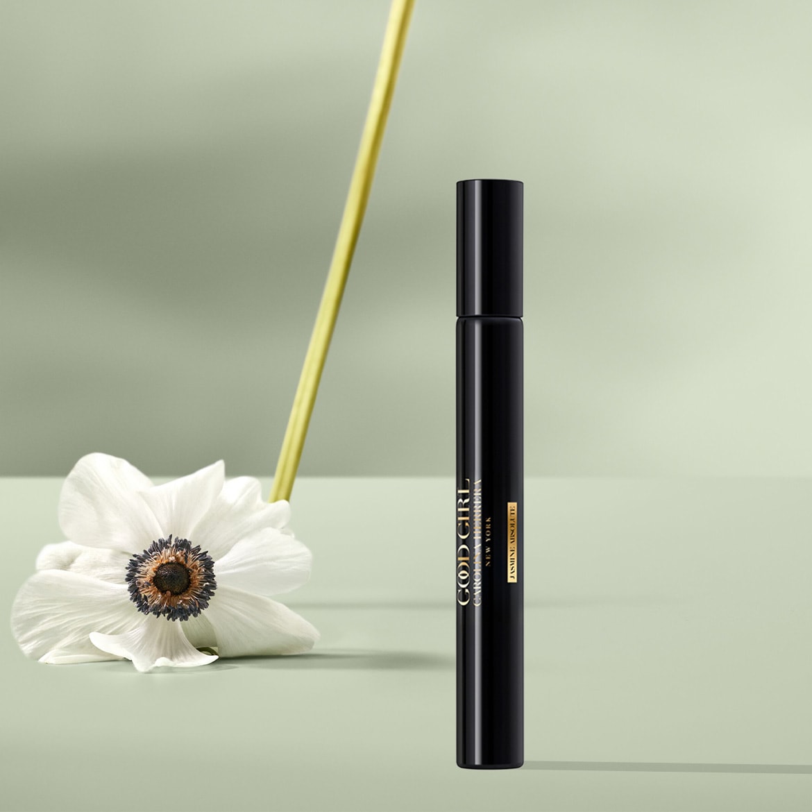 Eine schwarze Good Girl Carolina Herrera New York Jasmine Absolute Parfümflasche steht neben einer weißen Blume mit einem gelben Stiel.