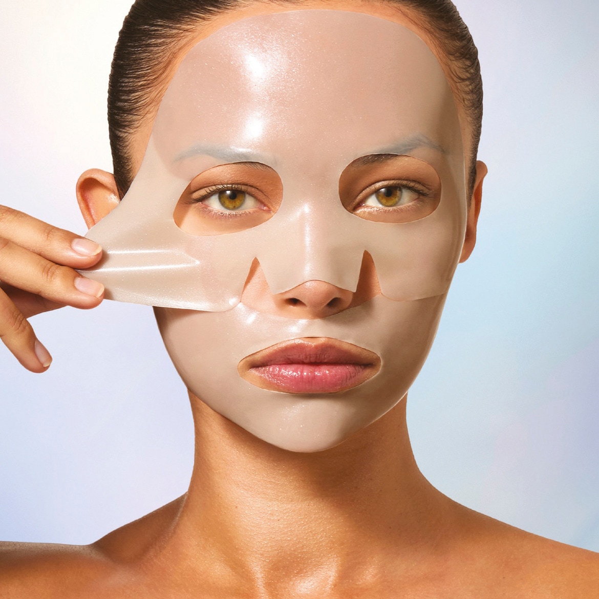 Eine Frau mit glänzender Haut zieht eine transparente Gesichtsmaske von ihrem Gesicht ab, die ihre Augen, Nase und Mund freilässt.