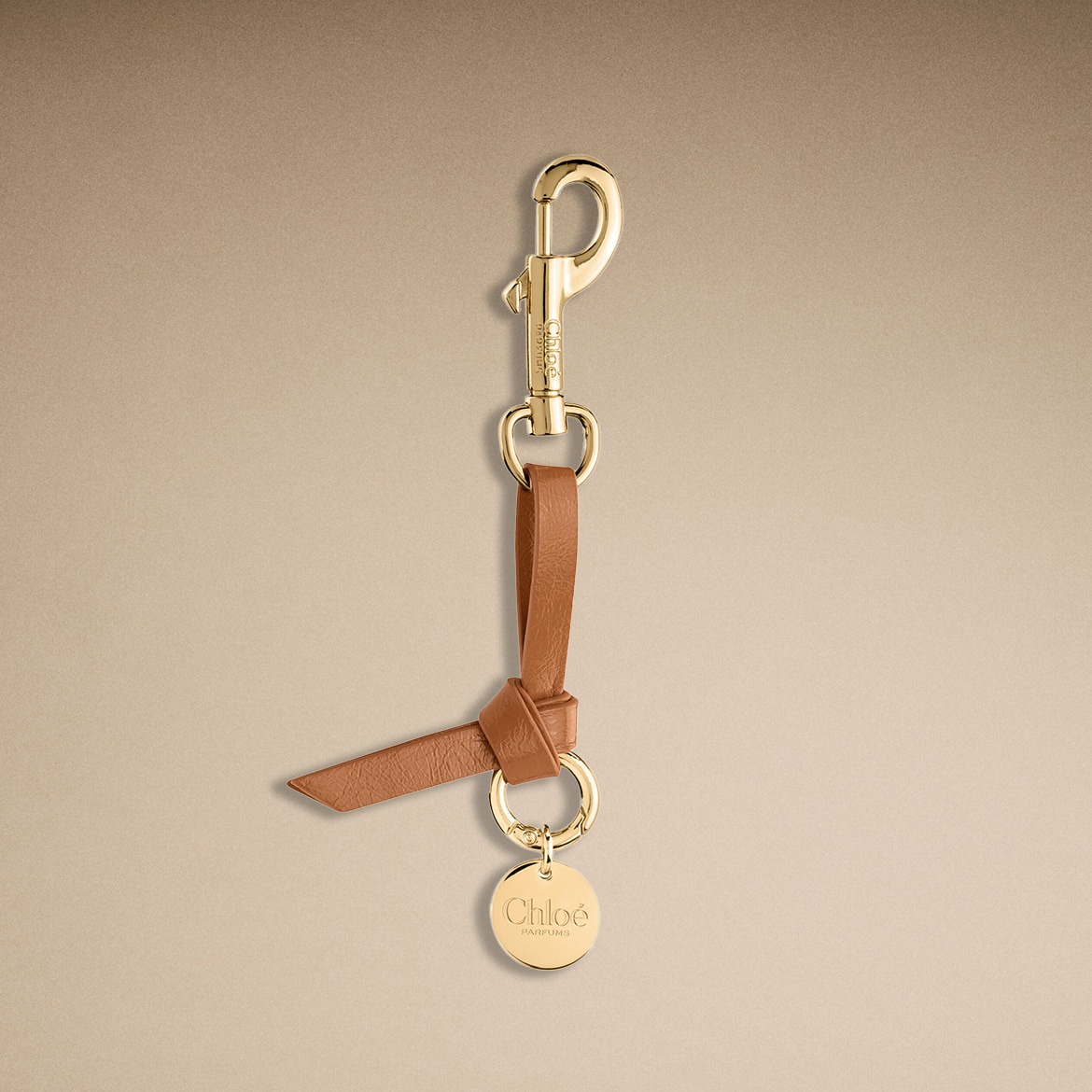 Der goldene Schlüsselanhänger von Chloé Parfums ist mit einem braunen Lederband und einem runden Anhänger mit dem Chloé-Logo verziert.