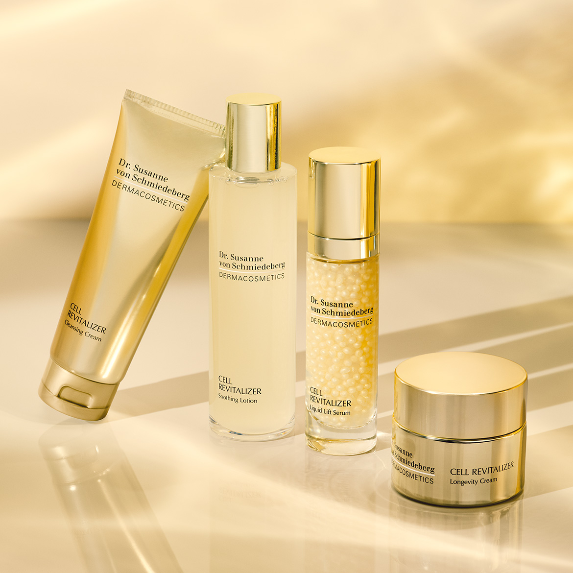 Entdecken Sie die Dr. Susanne von Schmiedeberg Cell Revitalizer Pflegeserie, bestehend aus einer Cleansing Cream, Soothing Lotion, Liquid Lift Serum und Longevity Cream, alle in eleganten goldfarbenen Verpackungen.