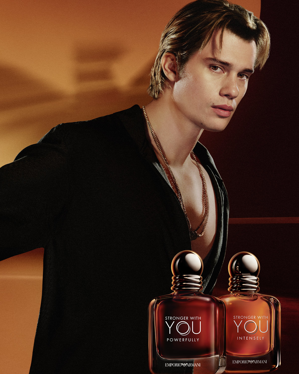 Ein junger Mann mit blonden Haaren und goldenen Ketten präsentiert die Duftkollektion "Stronger With You" von Emporio Armani, bestehend aus den Varianten "Powerfully" und "Intensely".