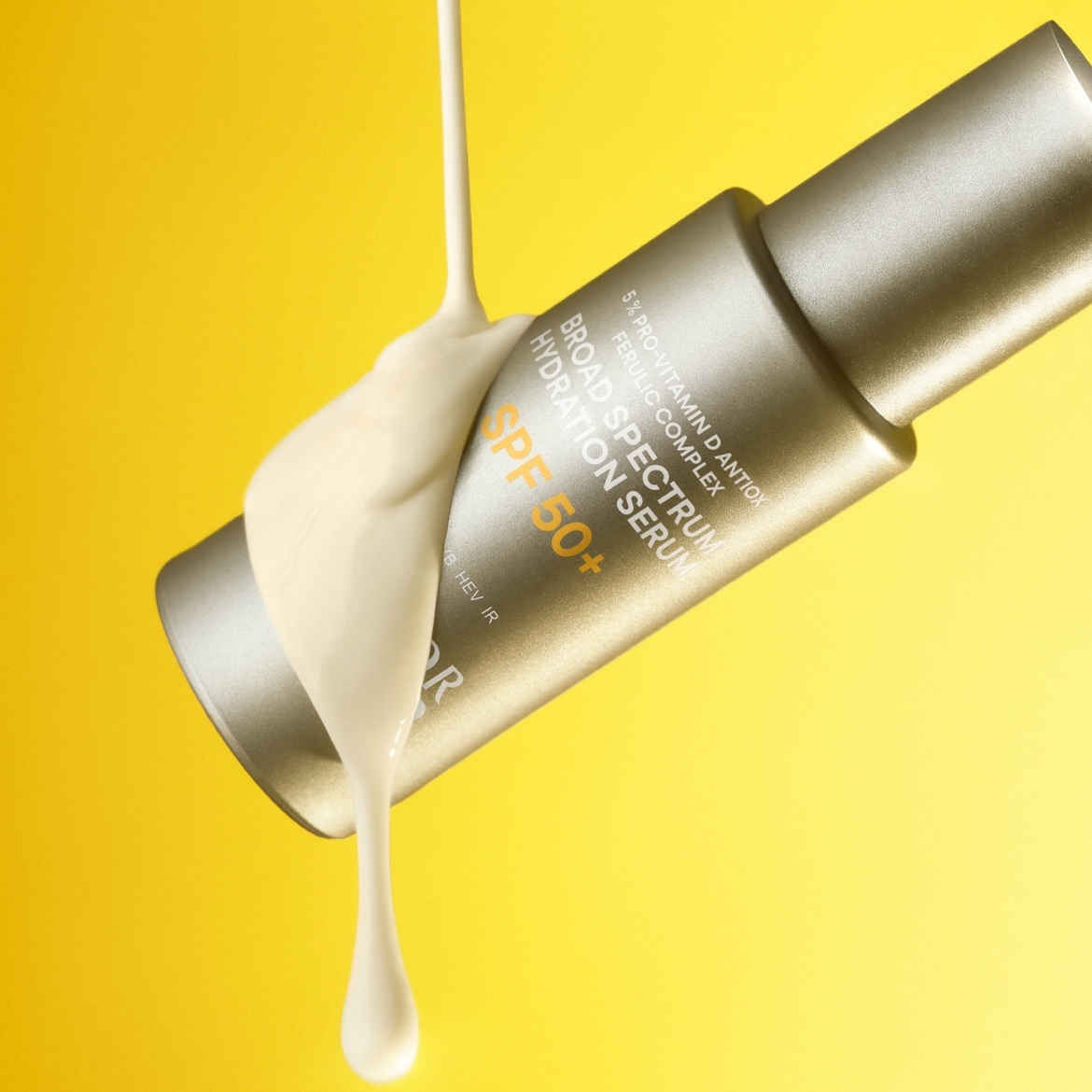 Auf gelbem Hintergrund ist eine Tube Sonnenschutzserum mit SPF 50+ zu sehen, auf die eine cremefarbene Flüssigkeit gegossen wird, die die Textur und den Schutz des Produkts hervorhebt.