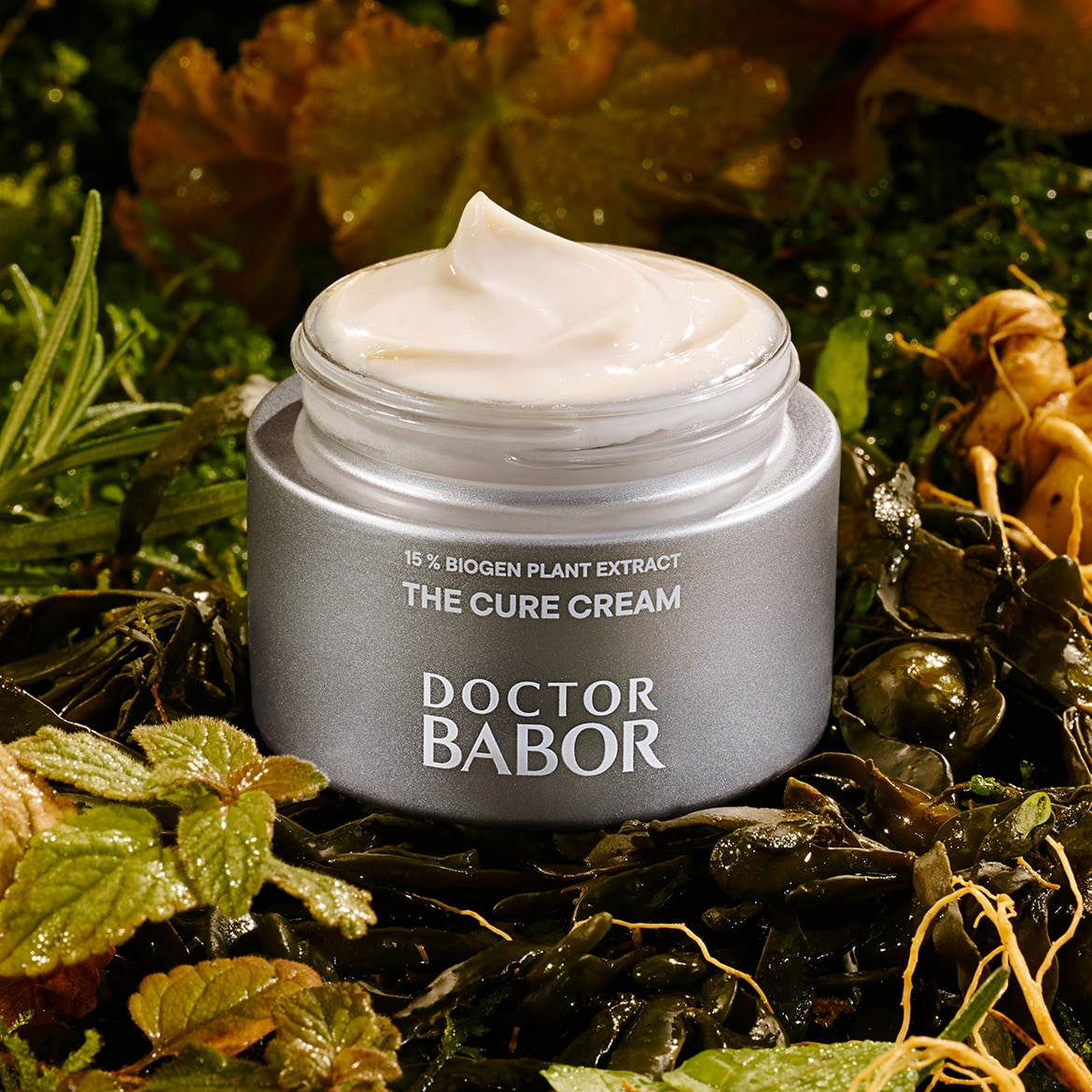 Nahaufnahme von Doctor Babor The Cure Cream mit 15 % Biogen-Pflanzenextrakt in einem silbernen Tiegel, umgeben von üppigem Grün.