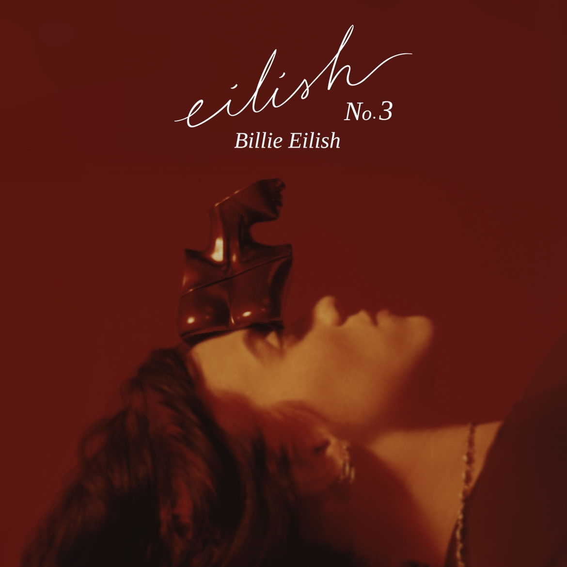 Das Bild zeigt Billie Eilish No. 3 Duft mit einer Skulptur auf dem Kopf der Person, die das Produkt bewirbt, vor einem roten Hintergrund.