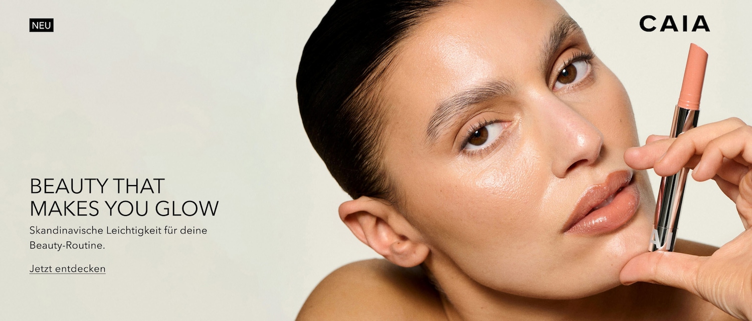 Nahaufnahme eines Models mit glänzender Haut, das einen Lippenstift der Marke CAIA in der Hand hält, daneben der Text "Beauty that makes you glow. Skandinavische Leichtigkeit für deine Beauty-Routine. Jetzt entdecken".