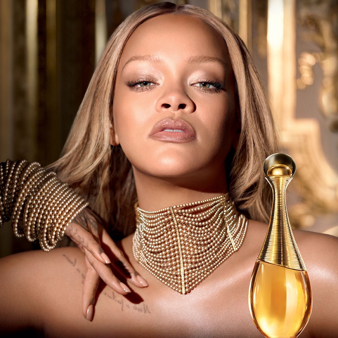 Rihanna präsentiert J'adore Eau de Parfum in einem goldenen Flakon, geschmückt mit einer Halskette aus goldenen Perlen, die Eleganz und Luxus ausstrahlt.