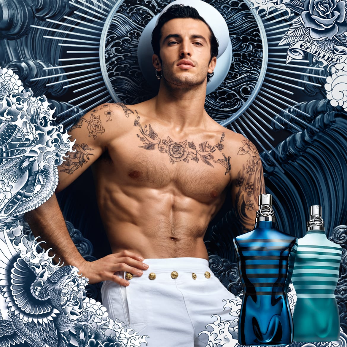 Ein tätowierter Mann mit Matrosenmütze posiert neben zwei Jean Paul Gaultier Flakons in Form von Männerkörpern, der eine in Blau mit schwarzen Streifen, der andere in Türkis mit weißen Streifen.