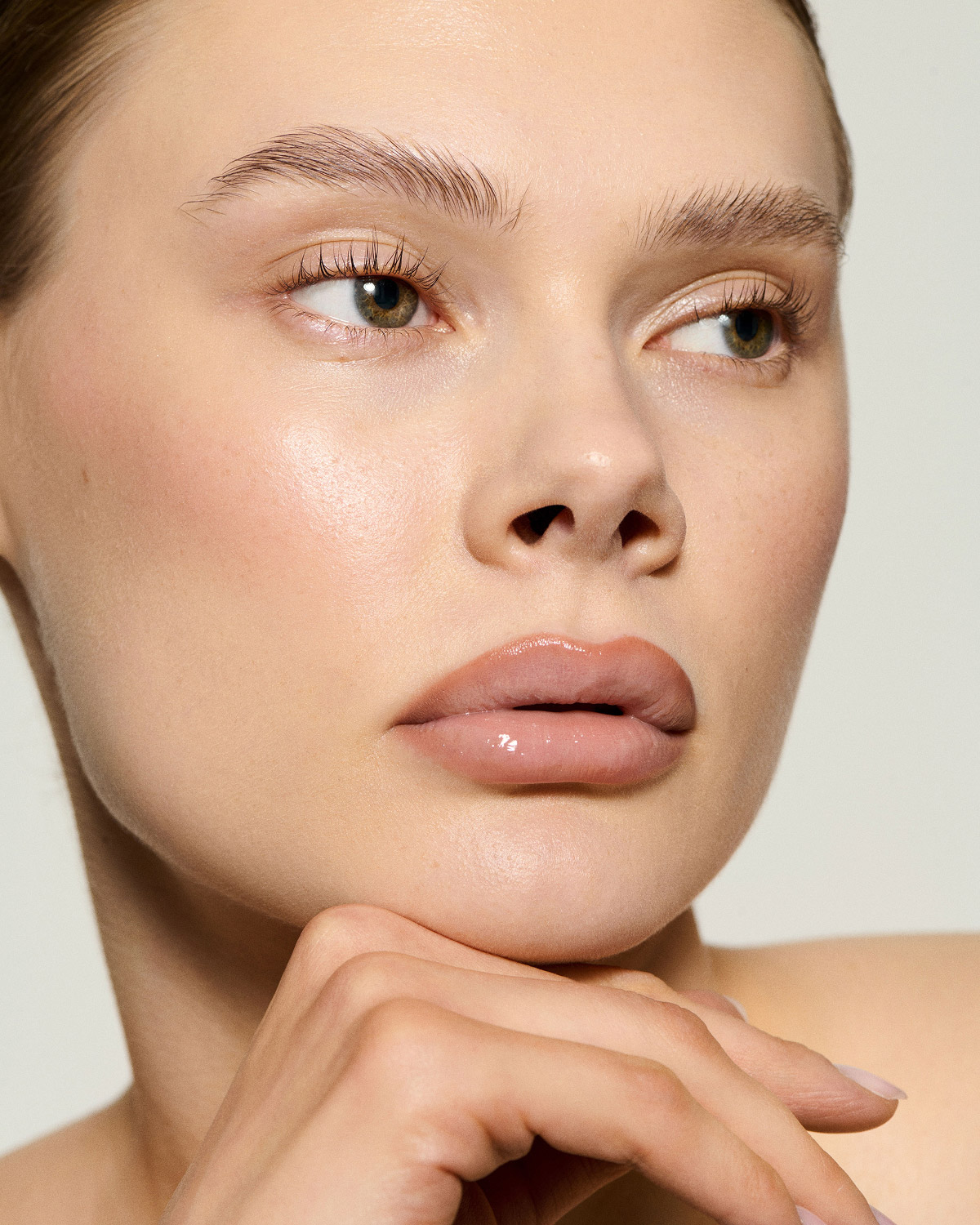 Nahaufnahme eines Frauengesichts mit natürlichem Make-up, die ihre Hand unter ihr Kinn legt und zur Seite schaut.