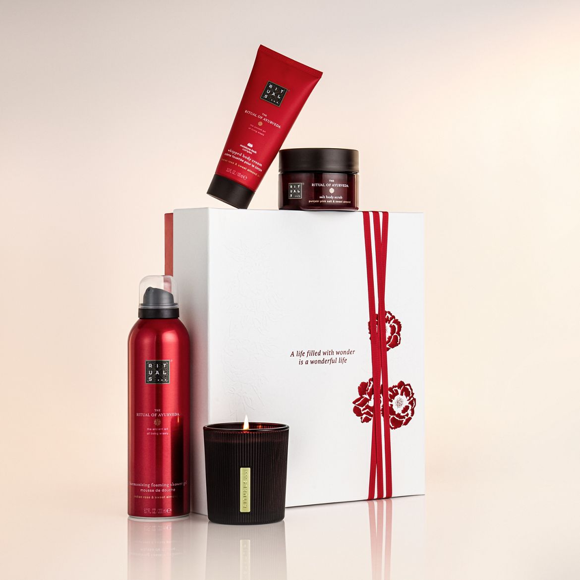 Das Ritual von Ayurveda Set mit roter Verpackung beinhaltet Körpercreme, Duschgel, Körperpeeling und Duftkerze, präsentiert in einer weißen Geschenkbox mit roter Schleife und Blumenmuster.