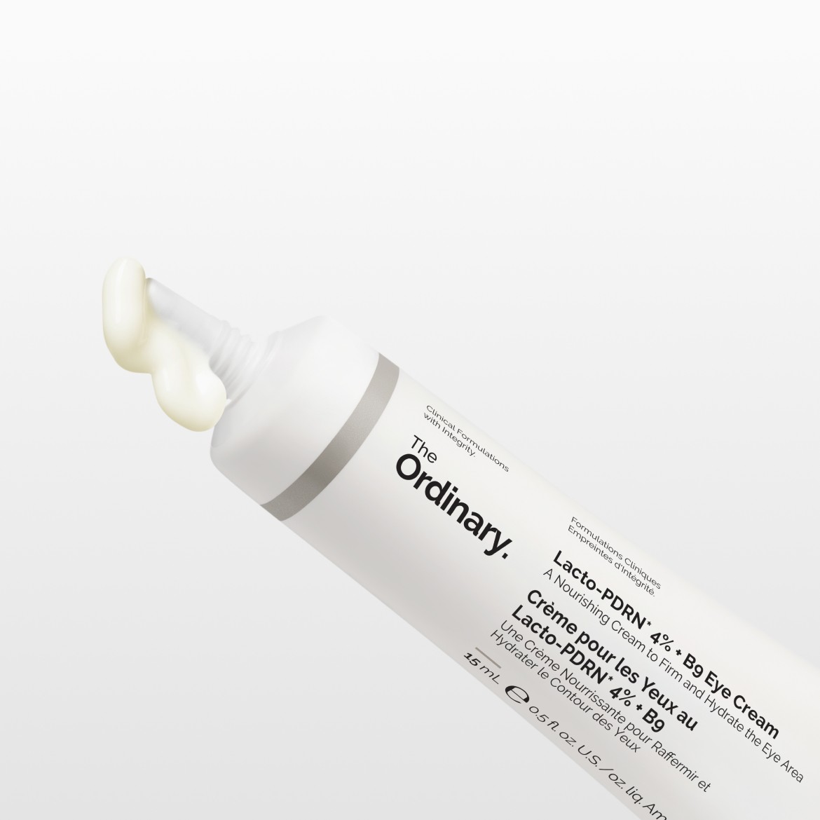 Die The Ordinary Lacto-PDRN 4% + B9 Augencreme in einer weißen Tube mit grauen Akzenten, aus der eine hellgelbe Creme austritt, ist eine nährende Creme zur Straffung und Hydratation der Augenpartie.
