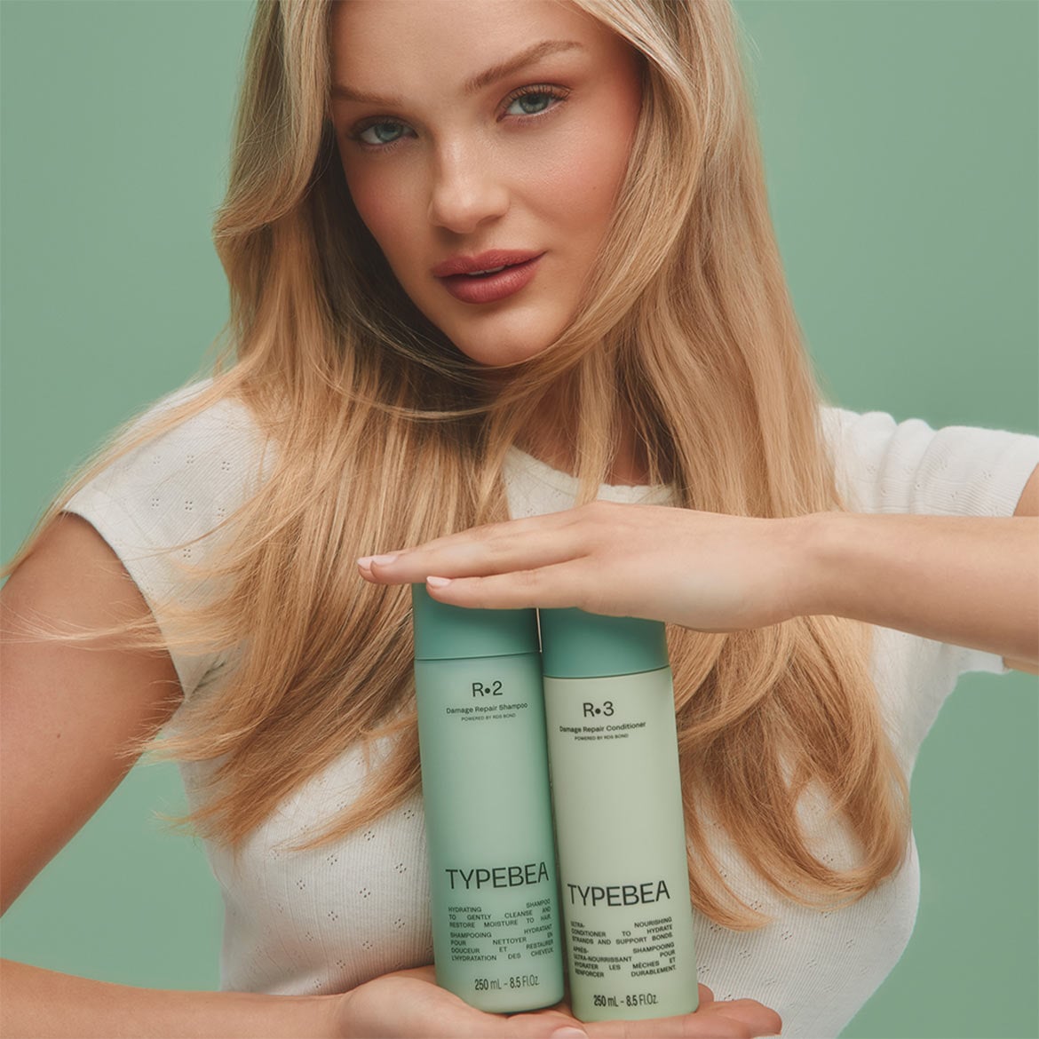 Eine blonde Frau hält zwei mintgrüne Flaschen von Typebea R.2 Damage Repair Shampoo und R.3 Damage Repair Conditioner in ihren Händen, die jeweils 250 ml Inhalt haben.