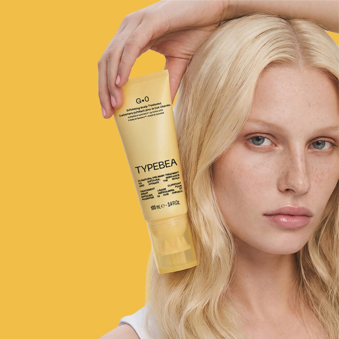 Eine Frau mit blondem Haar hält eine gelbe Tube TYPEBEA G.0 Peeling-Kopfhautbehandlung in der Hand, die 100 ml enthält und für die Klärung, das Peeling und die Hydratation der Kopfhaut entwickelt wurde.