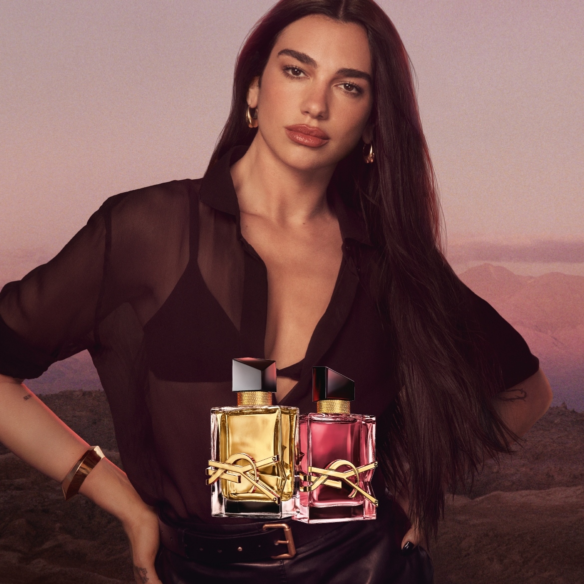 Dua Lipa präsentiert zwei YSL Libre Düfte: einen goldenen und einen pinkfarbenen Flakon mit dem ikonischen YSL-Logo, die sinnliche Freiheit und moderne Eleganz verkörpern.