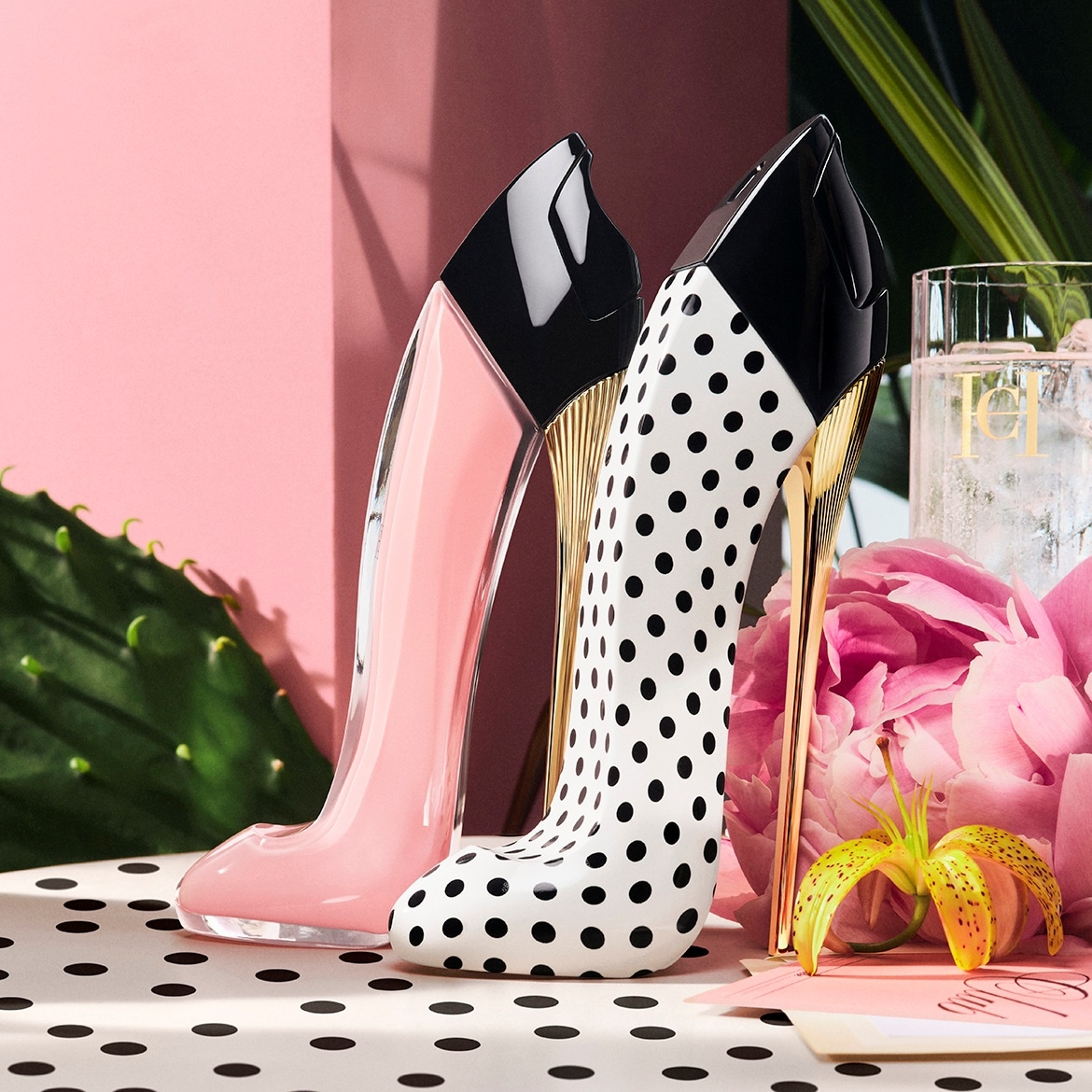 Zwei High-Heel-förmige Parfümflaschen, eine rosa und die andere weiß mit schwarzen Punkten, stehen auf einem Tisch mit Blumen.