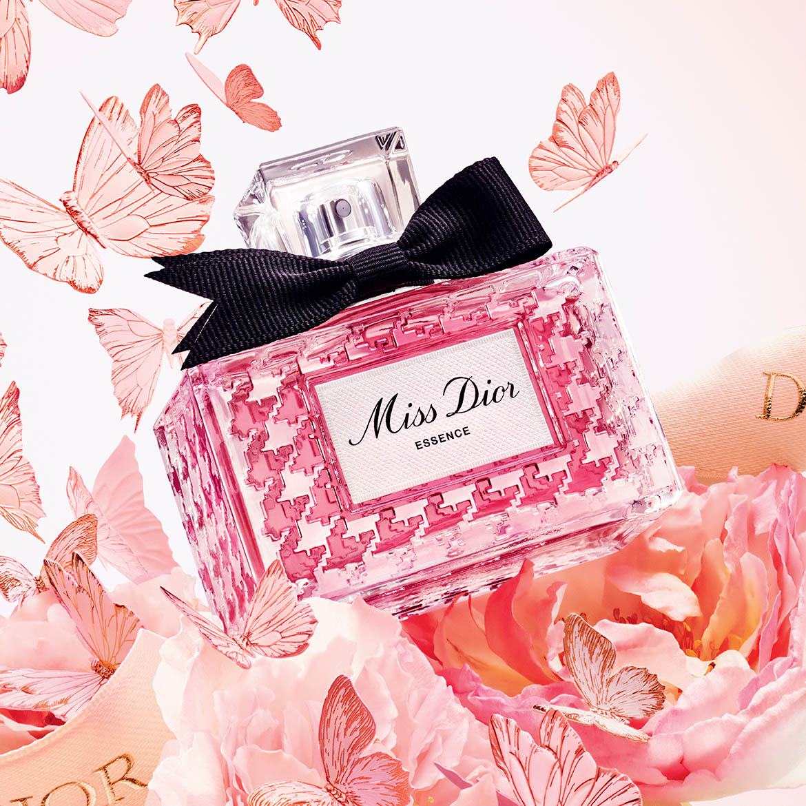 Ein rechteckiger, rosa Miss Dior Essence-Flakon mit einer schwarzen Schleife auf einem Bett aus rosa Blumen und rosa Schmetterlingen.