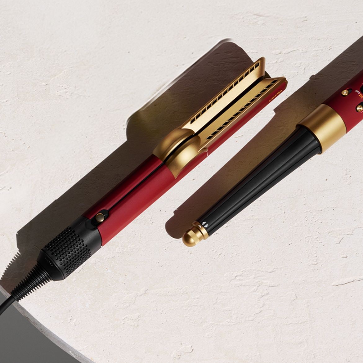 Nahaufnahme eines roten und goldenen Lockenstabs mit schwarzem Kabel auf einem hellen Untergrund, der zum Stylen der Haare bereit ist.