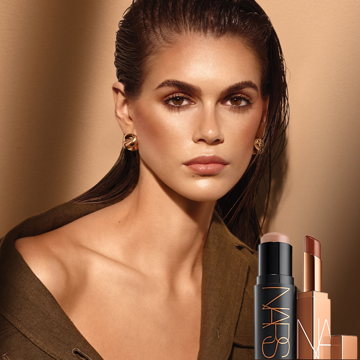 Nahaufnahme eines Models mit nassen Haaren, goldenen Ohrringen und einem grünen Blazer, neben dem zwei NARS-Produkte stehen: ein schwarzer Stick und ein goldener Lippenstift.