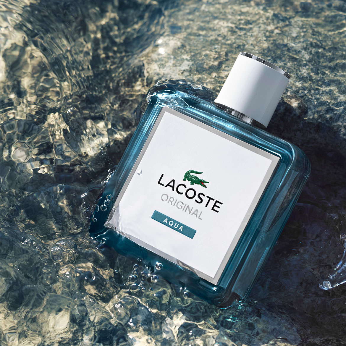 Das Lacoste Original Aqua Eau de Toilette präsentiert sich in einem hellblauen Glasflakon mit weißem Etikett, das den Lacoste-Schriftzug und das Krokodil-Logo zeigt, während es im Wasser liegt.