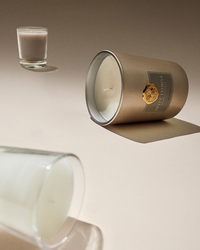 Zwei Duftkerzen von Douglas und Molton Brown stehen vor einem Hintergrund aus Holzstücken und Steinen, die eine warme und einladende Atmosphäre schaffen.