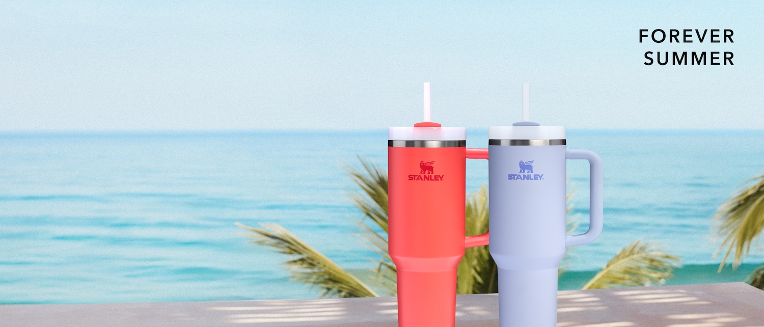 Vor dem Hintergrund eines ruhigen Ozeans stehen zwei Stanley-Becher, einer in Koralle und einer in Lavendel, die die Aufschrift „Forever Summer“ tragen.