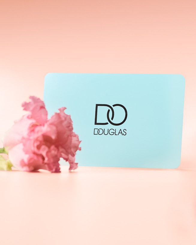 Eine hellrosa Karte mit den Worten „DANKE, MAMA“ in fetten schwarzen Buchstaben, verziert mit einer kleinen rosa Blume und einer türkisfarbenen Douglas-Geschenkkarte, die mit einem goldenen Band umbunden ist.