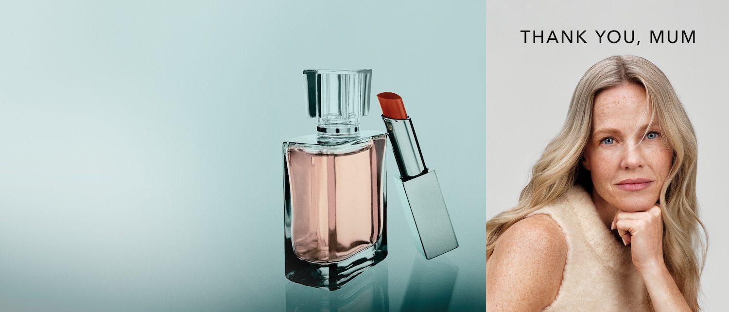 Ein elegantes Stillleben zeigt einen Parfümflakon mit rosa Flüssigkeit und einen silbernen Lippenstift mit roter Spitze, daneben das Porträt einer blonden Frau mit dem Schriftzug „DANKE, MAMA“.