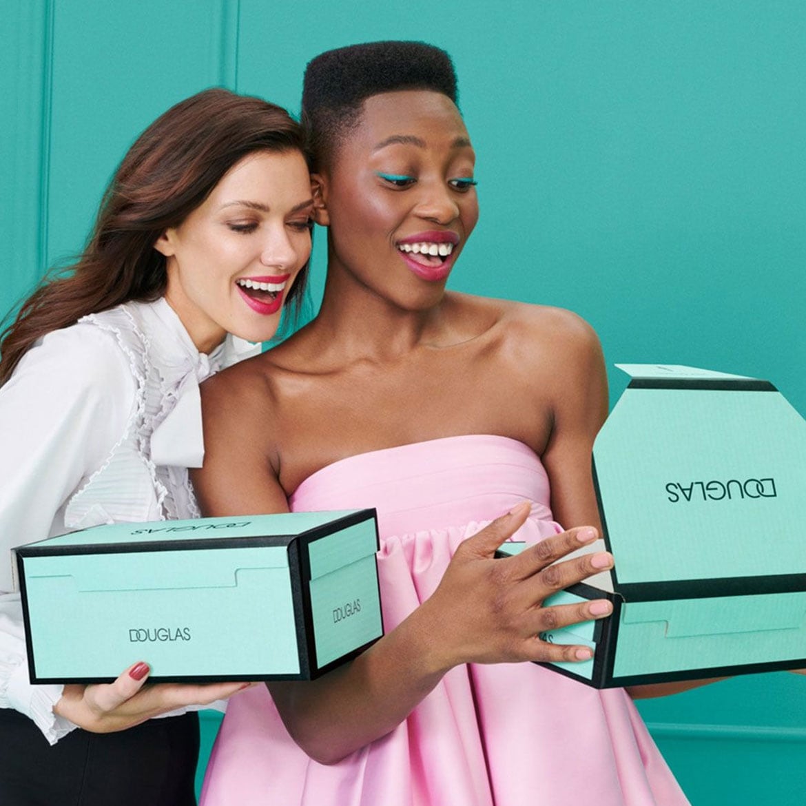 Zwei Frauen freuen sich über Douglas-Geschenke in hellblauen Boxen, die mit schwarzen Akzenten versehen sind.