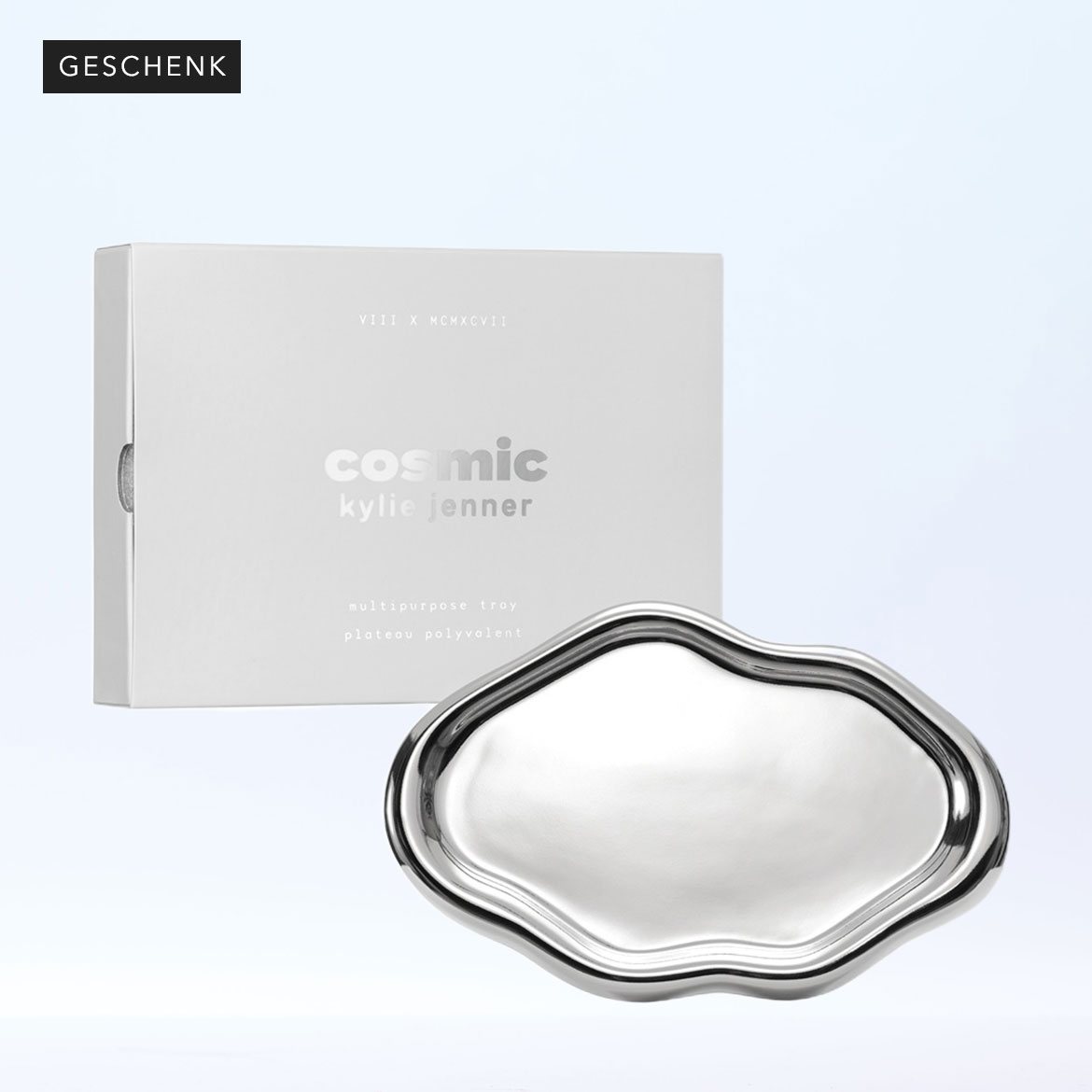 Präsentiert wird ein silbernes, wellenförmiges Mehrzwecktablett von Cosmic Kylie Jenner, zusammen mit seiner Verpackung in einer hellgrauen Schachtel.