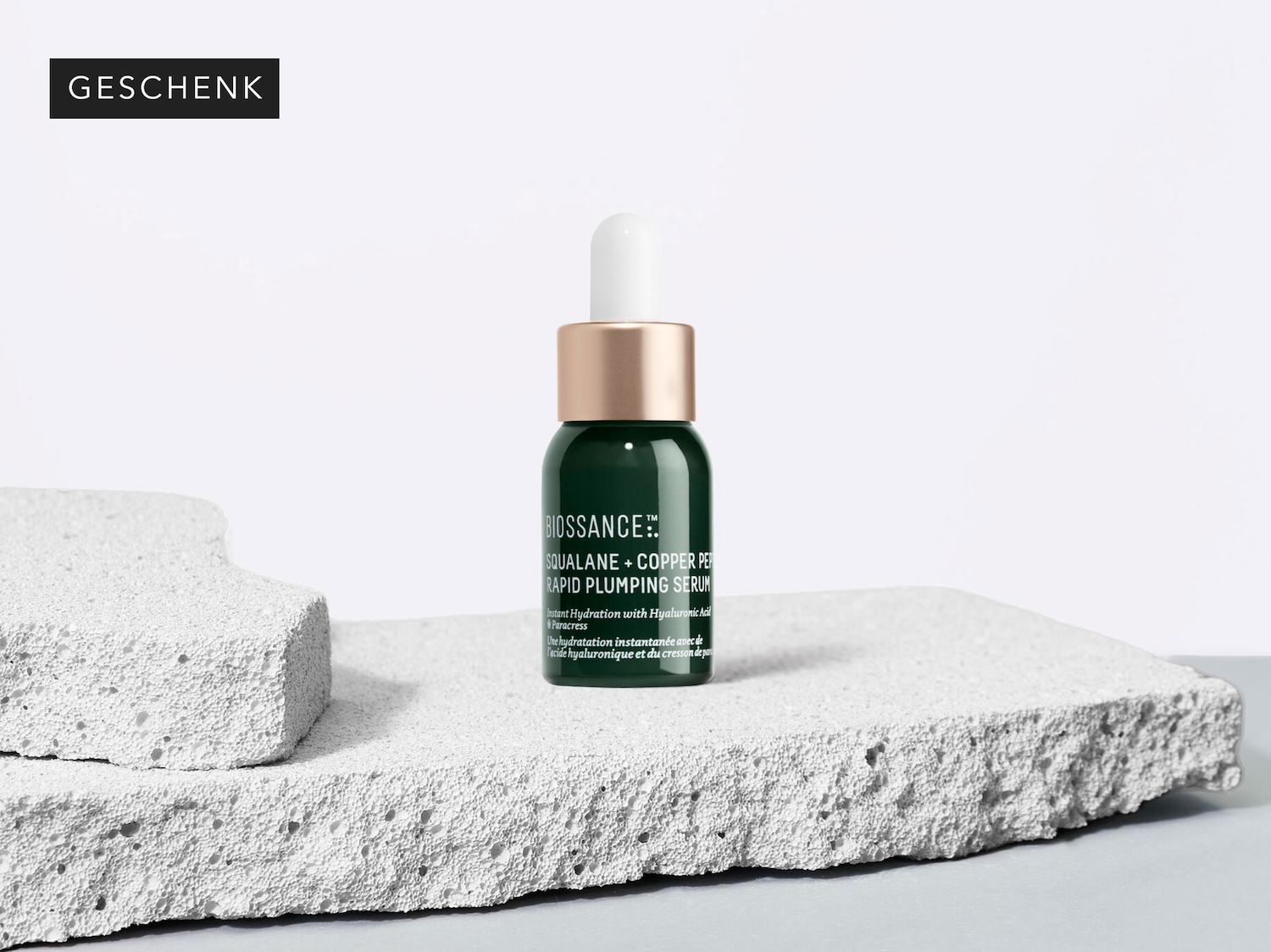 Here’s a Biossance Squalane + Copper Peptide Rapid Plumping Serum in a dark green bottle with a white dropper, presented as a ‘GESCHENK’ or gift.