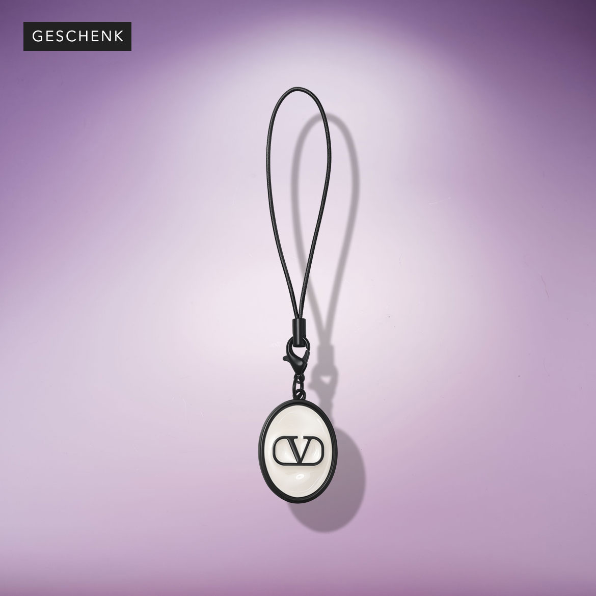 Schwarzer Schlüsselanhänger mit dem Valentino-Logo an einem schwarzen Band vor einem violetten Hintergrund.