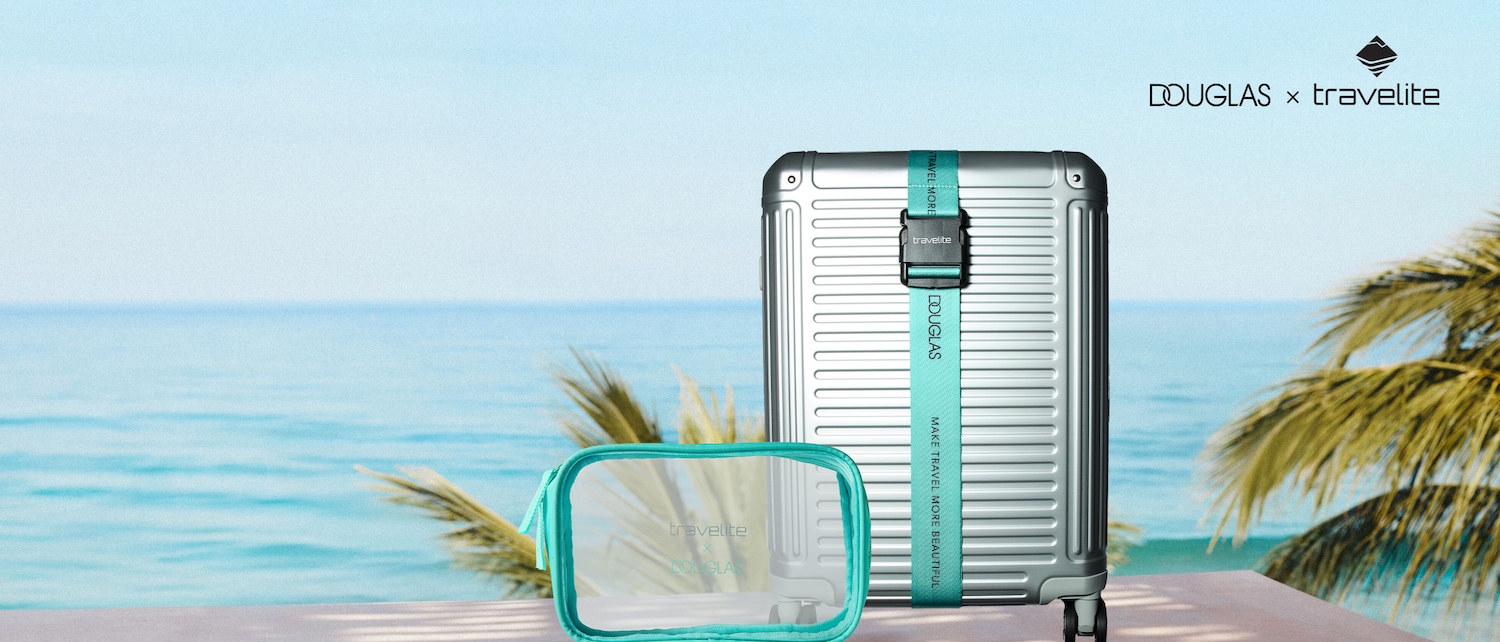 Vor einem Hintergrund aus blauem Meer und Palmen steht ein silberner Douglas x Travelite Koffer mit einem türkisfarbenen Gurt und eine transparente Kosmetiktasche mit türkisfarbenen Akzenten.
