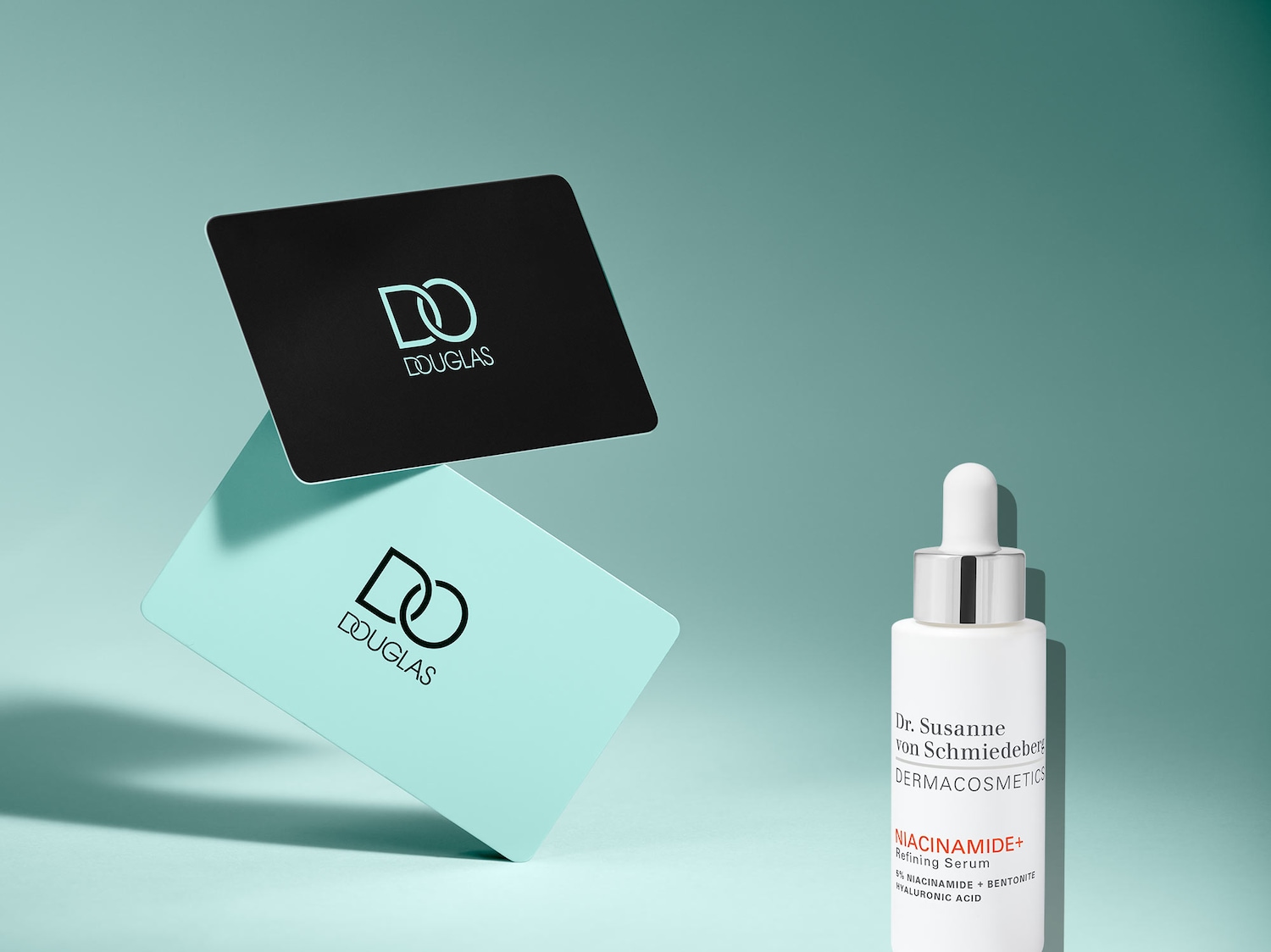 Two Douglas cards, one black and one turquoise, are stacked next to a white bottle of Dr. Susanne von Schmiedeberg Niacinamide+ Refining Serum.