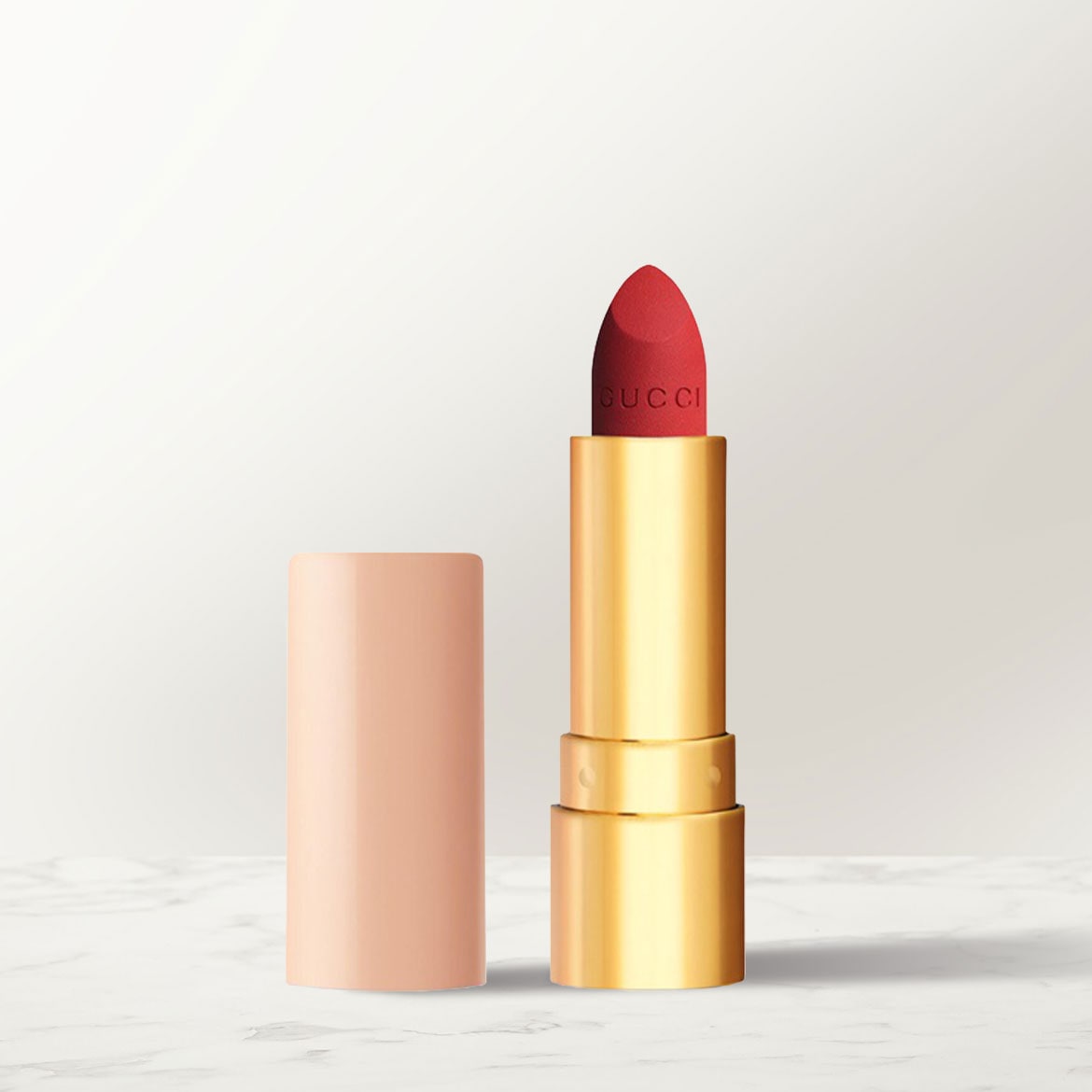 Dieser Gucci Lippenstift präsentiert sich mit einer roten Farbe und einem goldenen Gehäuse, während die abgenommene Kappe in einem zarten Pfirsichton gehalten ist.