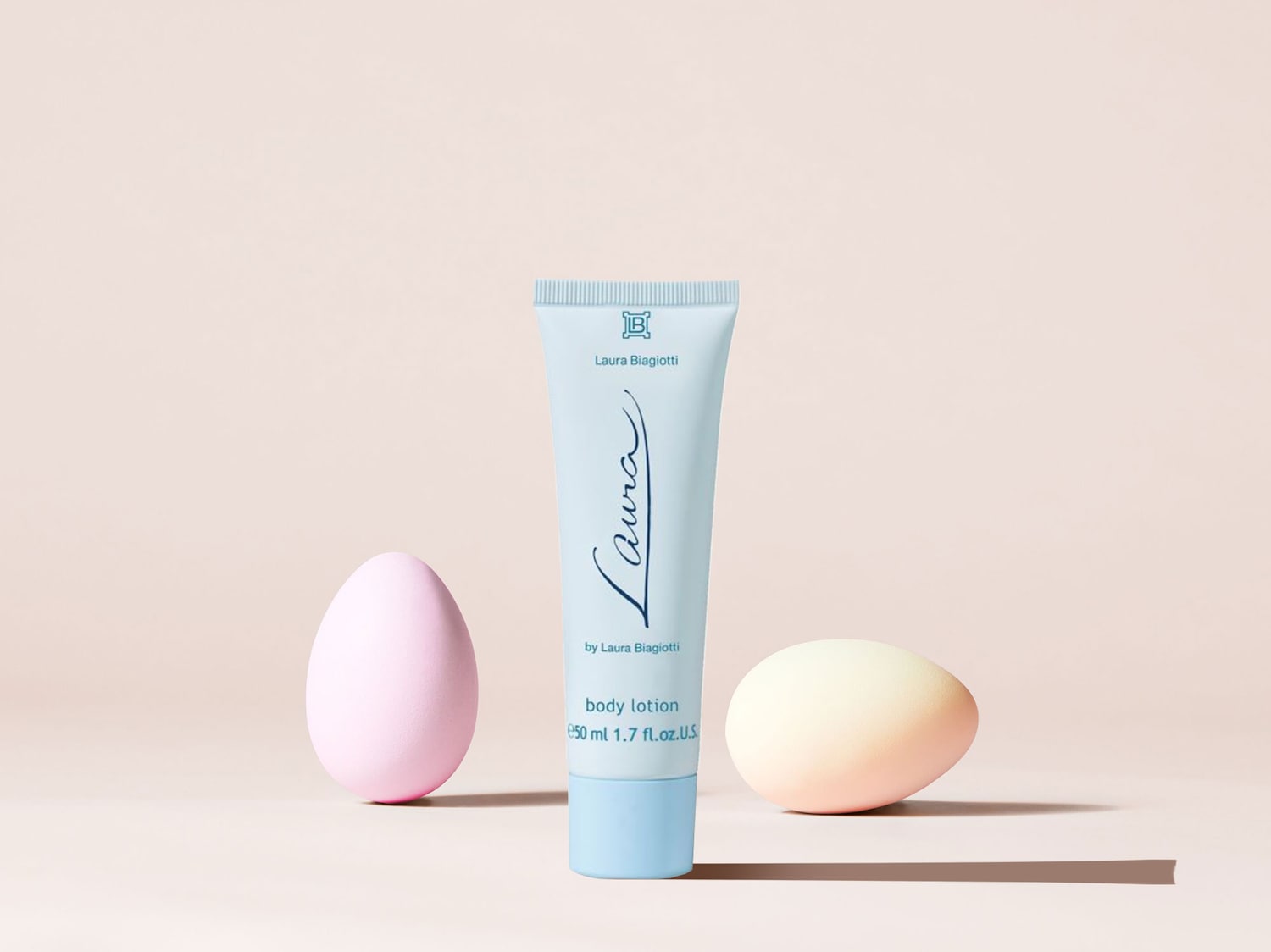 Die hellblaue Tube Laura Biagiotti Bodylotion mit dem Markennamen in kursiver Schrift steht zwischen einem rosa und einem gelben Osterei.