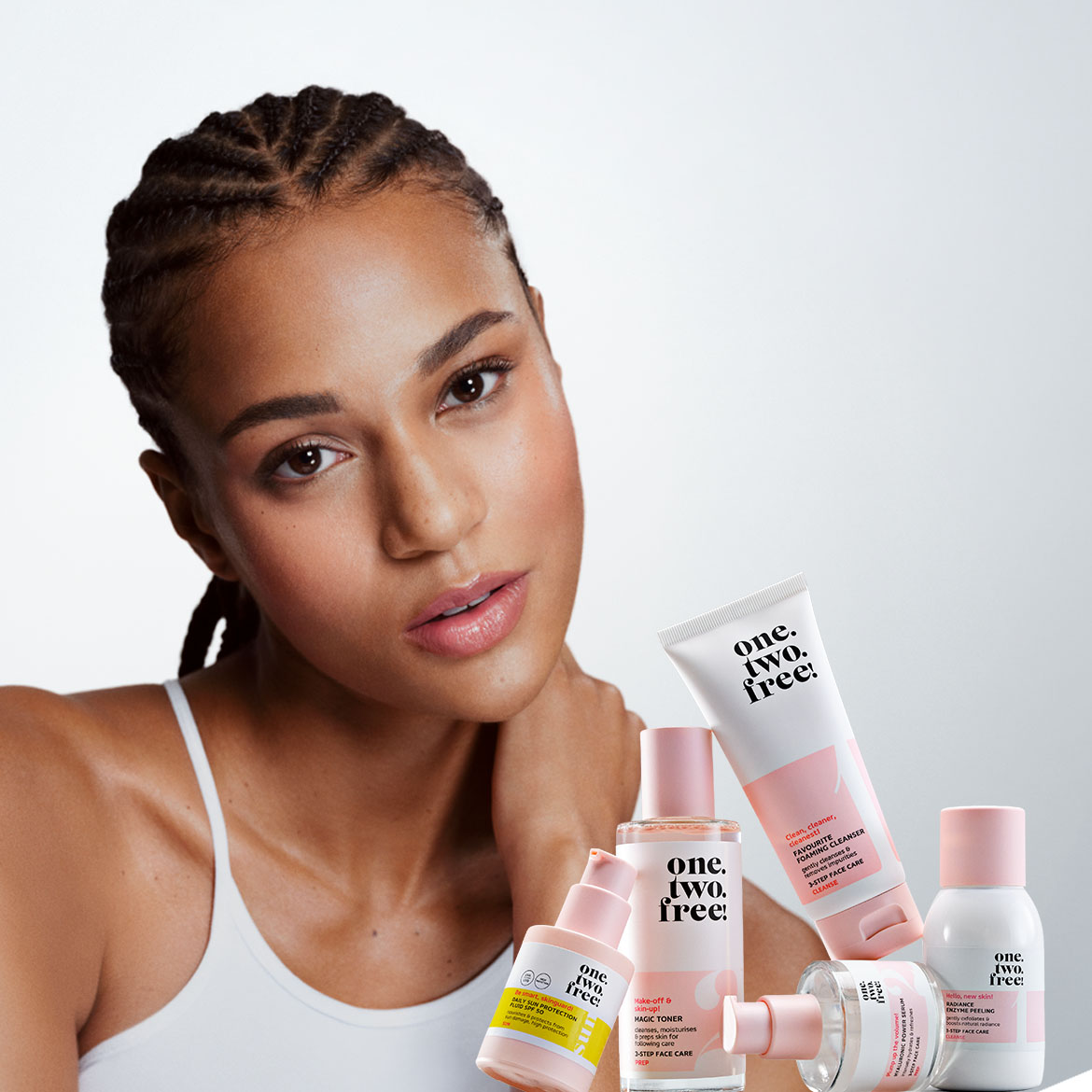 Entdecken Sie die "One. Two. Free!" Hautpflegeserie mit einer Frau, die die Produkte präsentiert, darunter Reinigungsschaum, Gesichtswasser, Sonnenschutz und Serum, alles für eine strahlende Haut.