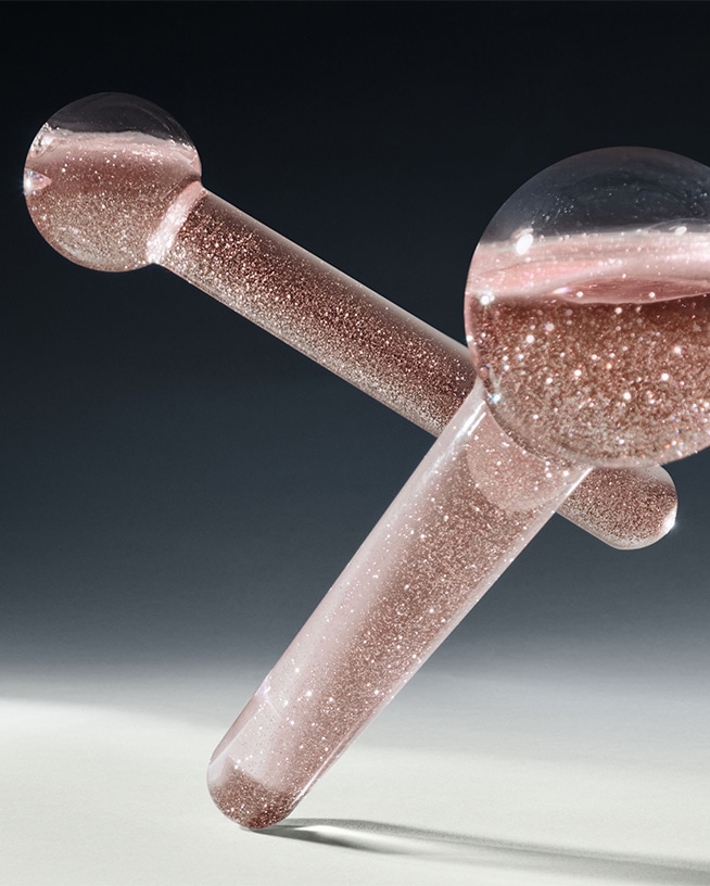 Nahaufnahme von zwei transparenten Massagegeräten mit rosa Flüssigkeit und Glitzerpartikeln, die zur Behandlung von Augenschatten verwendet werden können.