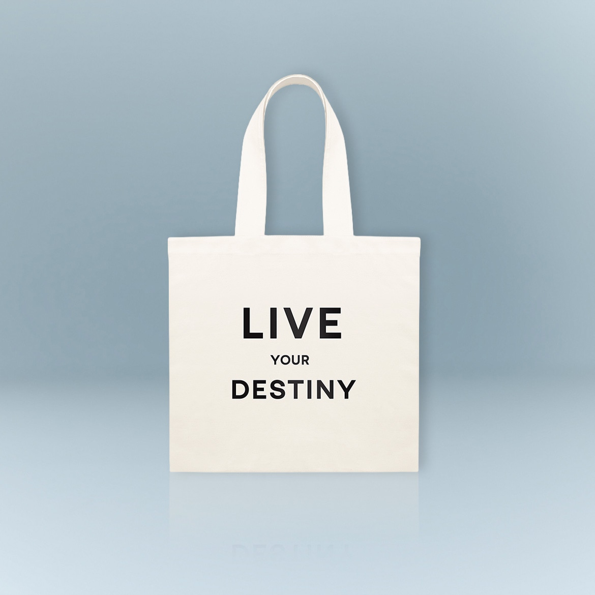 Eine weiße Stofftasche mit den Worten "Lebe deine Bestimmung" in schwarzer Schrift vor einem hellblauen Hintergrund.