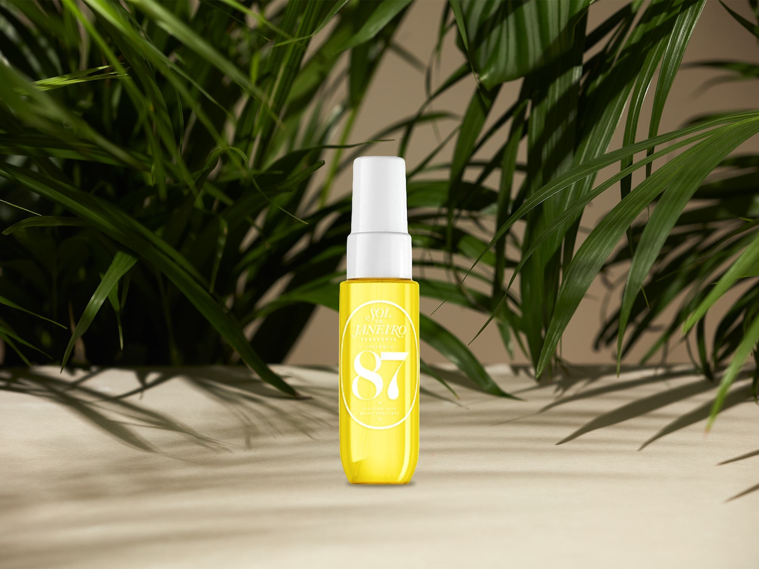 Gelbe Sol de Janeiro '87 Rio Radiance' Duftspray-Flasche mit weißer Kappe vor üppigem Grün.