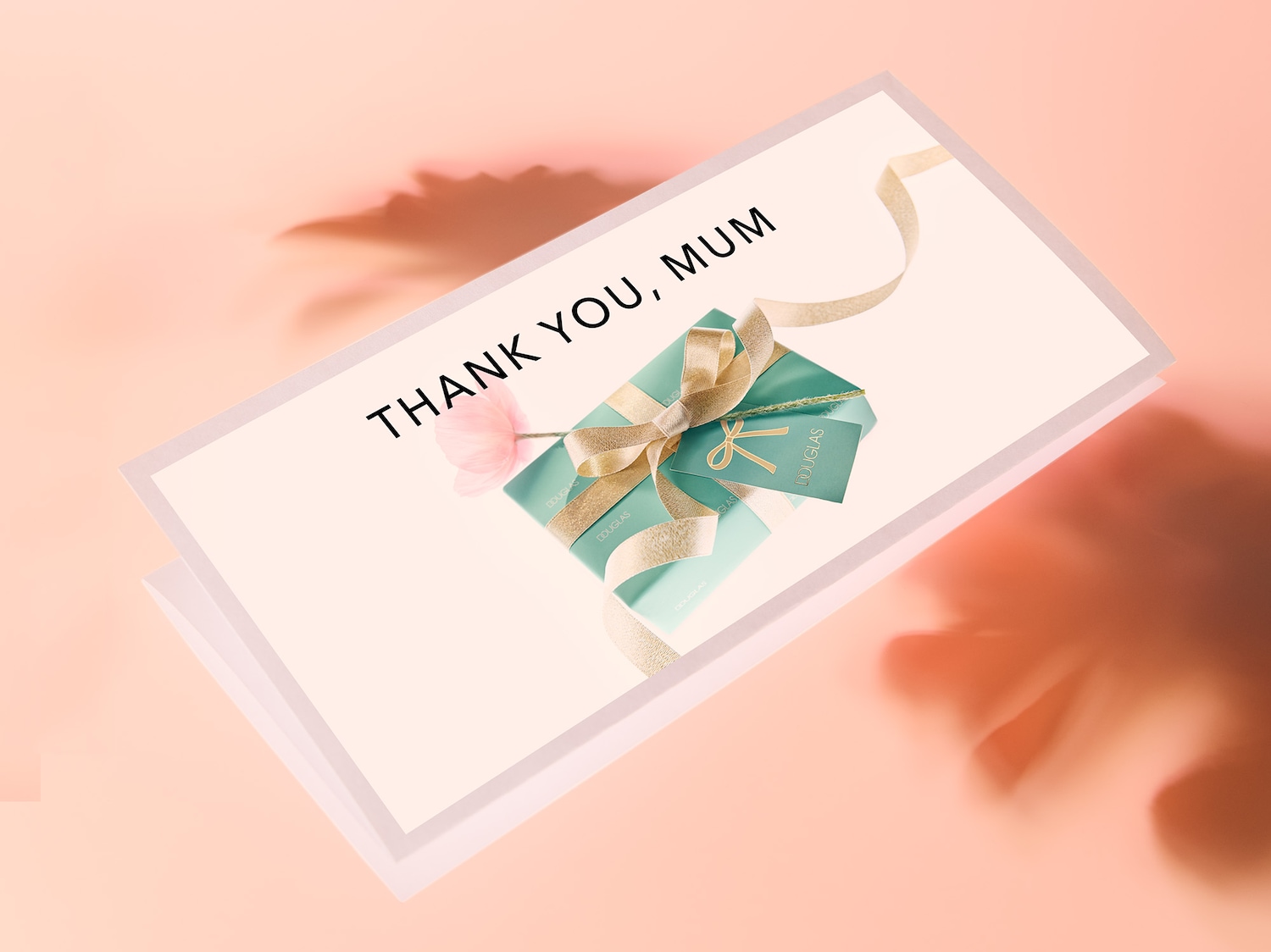 Eine Grußkarte mit der Aufschrift „DANKE, MAMA“ liegt auf einem rosa Hintergrund, darauf ein in Türkis verpacktes Geschenk mit goldener Schleife und Douglas-Logo.