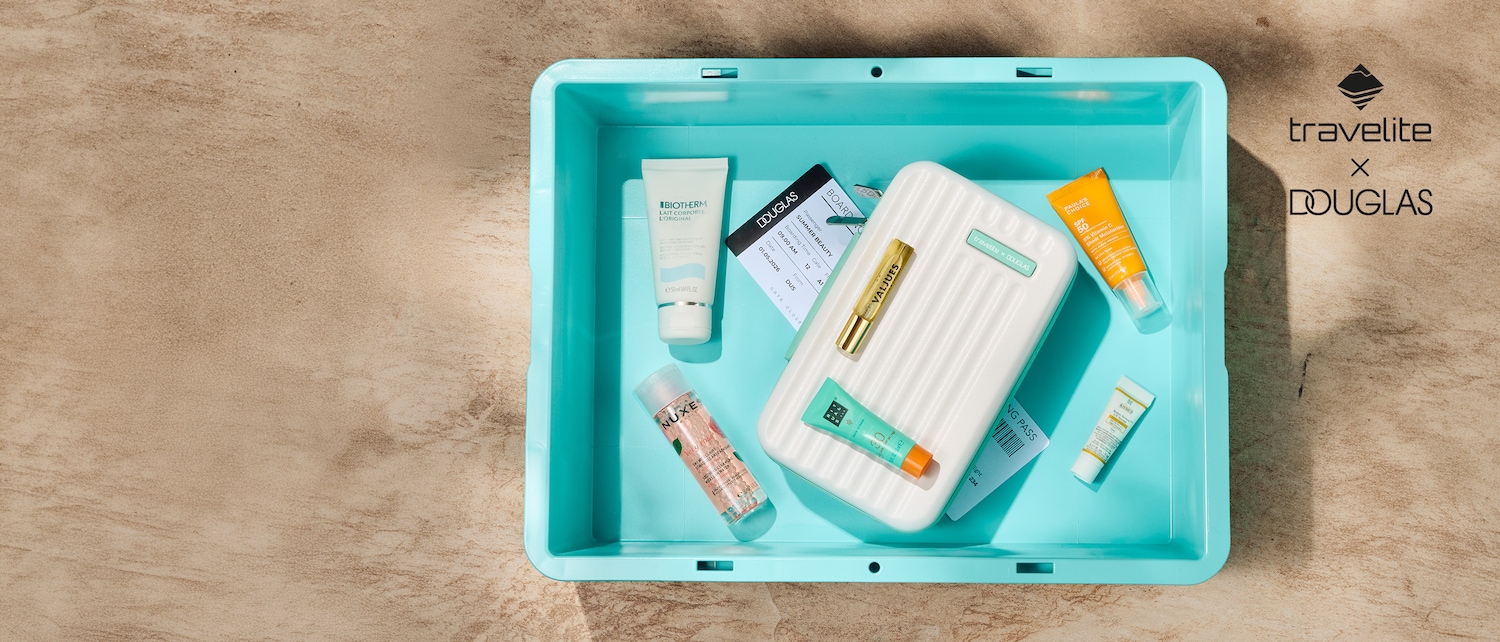 In einer hellblauen Schale liegen verschiedene Kosmetikprodukte wie Biotherm Lait Corporel, Nuxe Very Rose Gesichtswasser und Paula's Choice SPF 50, zusammen mit einem Boardingpass und einem Mini-Koffer von Travelite x Douglas.