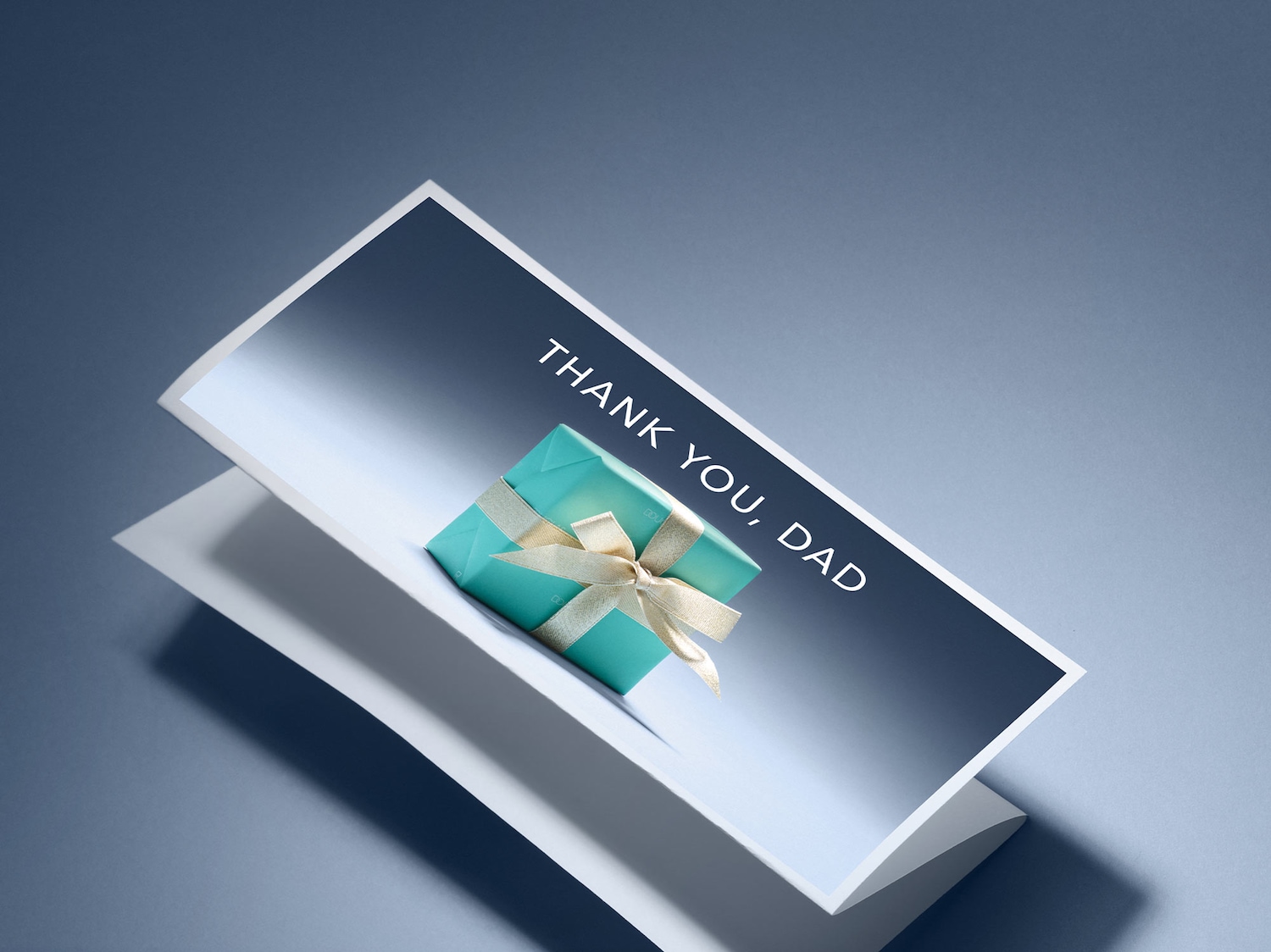 Ein hellblaues Geschenk mit einer goldenen Schleife liegt auf einer Karte mit der Aufschrift „DANKE, PAPA“.