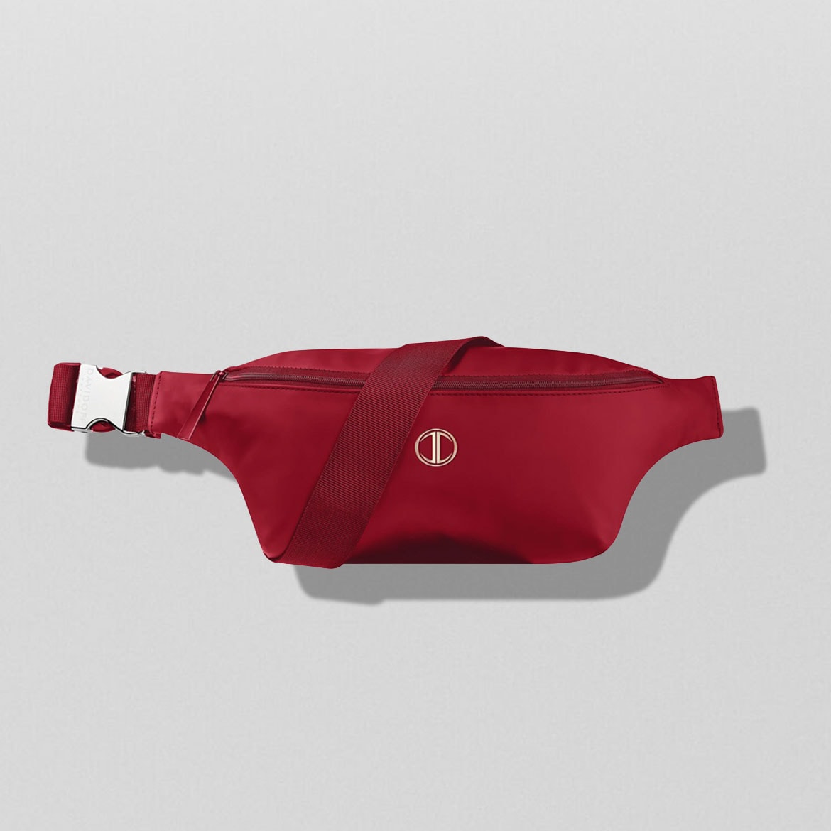 Eine rote Bauchtasche mit einem verstellbaren Riemen und einem silbernen Schnallenverschluss, die mit einem goldenen, kreisförmigen Logo verziert ist.