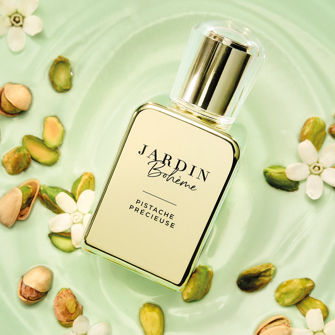 Der Duft von Jardin Bohème Pistache Précieuse in einem eleganten Flakon, umgeben von Pistazien und zarten weißen Blüten auf einem hellgrünen Hintergrund.