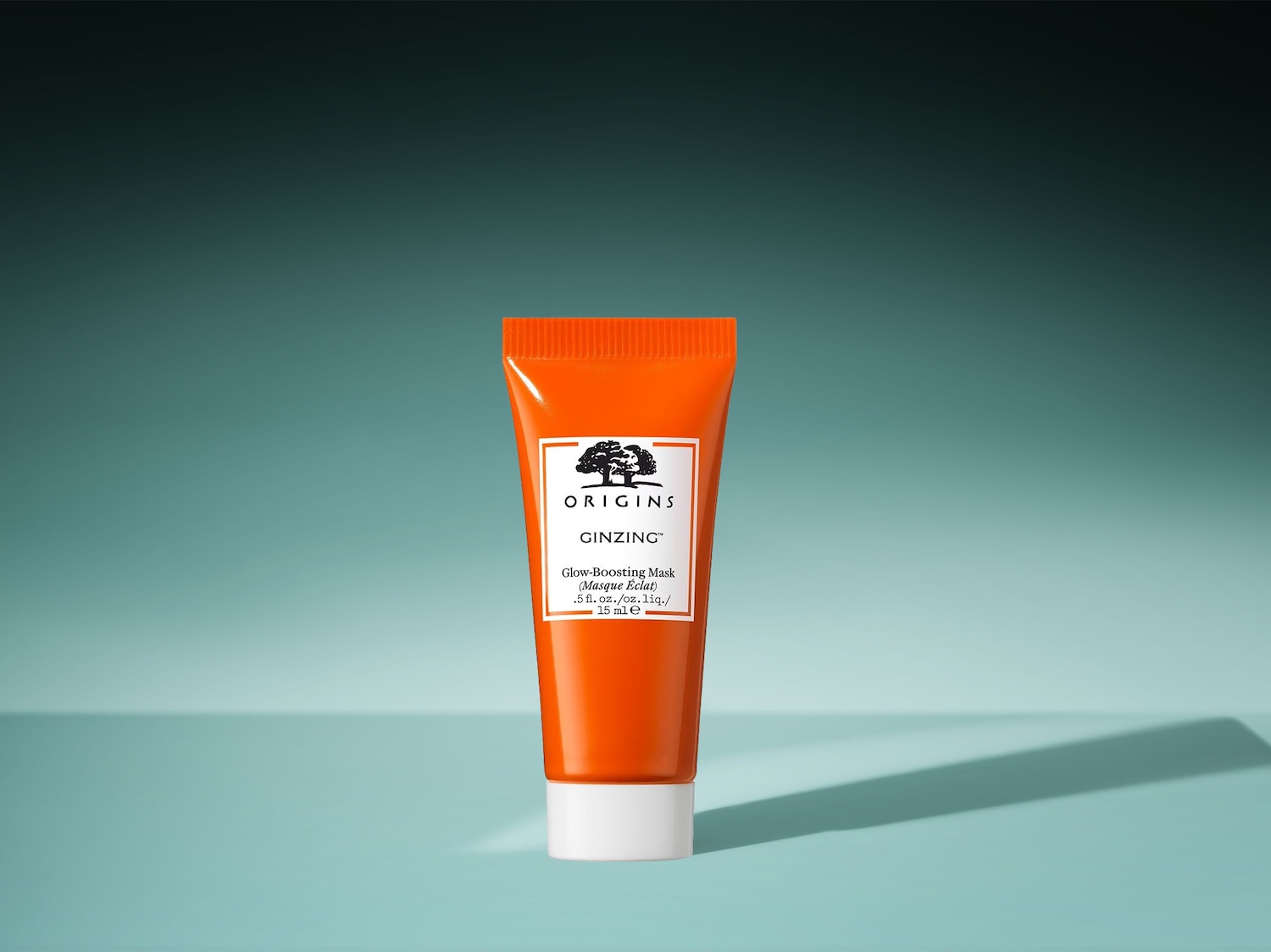 Die orangefarbene Tube Origins Ginzing Glow-Boosting Mask mit weißer Schrift und einem Baumlogo verspricht einen strahlenden Teint mit 15 ml Maske.
