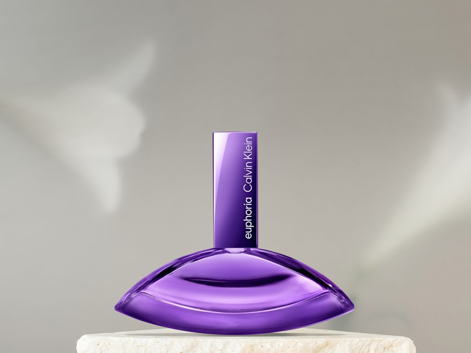 Ein Calvin Klein Euphoria Parfümflakon in leuchtendem Lila steht auf einem hellen Steinpodest vor einem weichen, grauen Hintergrund mit verschwommenen weißen Schatten.
