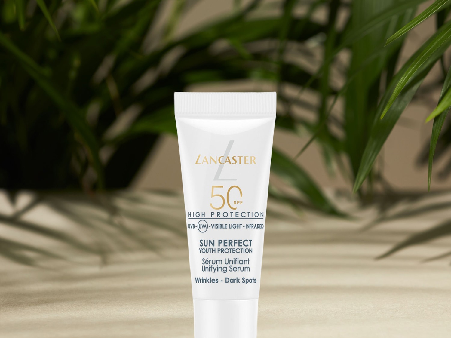 Die Lancaster Sun Perfect Youth Protection Unifying Serum mit LSF 50, in einer weißen Tube mit goldenem Logo, bietet hohen Schutz vor UVB-, UVA-, sichtbarem Licht und Infrarotstrahlung, während sie Falten und dunkle Flecken reduziert.