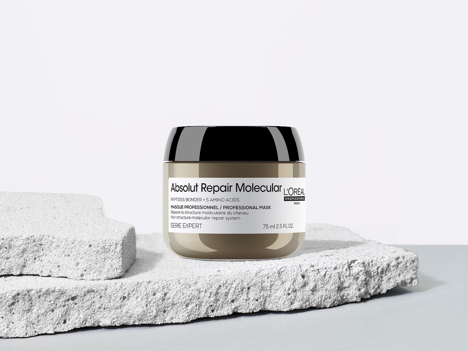 Die L'Oréal Professionnel Absolut Repair Molecular Maske in einem beigefarbenen Tiegel mit schwarzem Deckel, der 75 ml des Produkts enthält, steht auf zwei grauen, strukturierten Blöcken.