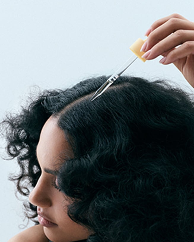 Eine Pipette trägt ein Pflegeprodukt direkt auf die Kopfhaut entlang eines Scheitels auf. Die Nahaufnahme steht für gezielte Scalp Care zur Unterstützung einer gesunden Kopfhaut und gepflegter Haare.